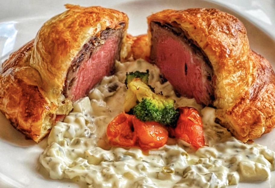 温かな灯が灯る自宅風のダイニングルームでスライスされたビーフウェリントン、延南パークを望む