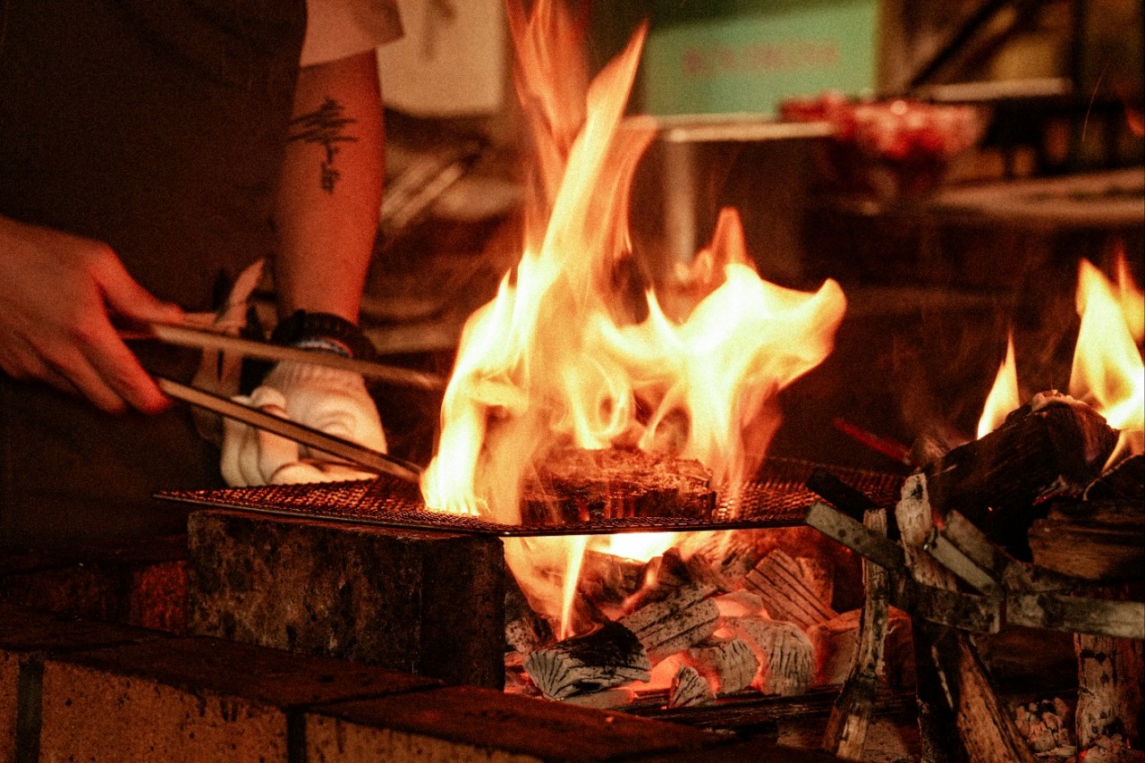 Ox Live Fire Grill wood-fire course with dancing flames and plated beef